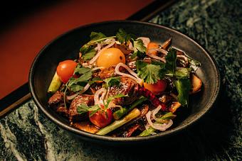 Product: A bowl of colorful stir-fry featuring cherry tomatoes, onion slices, cilantro, and assorted vegetables served on a dark plate. - Crying Tiger in Chicago, IL Restaurants/Food & Dining