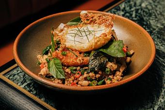Product: A black bowl filled with a savory dish, including crispy rice, green herbs, and vegetables, topped with a fried egg. - Crying Tiger in Chicago, IL Restaurants/Food & Dining