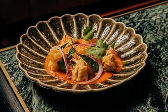 Product: Shrimp and Pork dumplings in a brown bowl with a rice orange sauce and herbs. - Crying Tiger in Chicago, IL Restaurants/Food & Dining