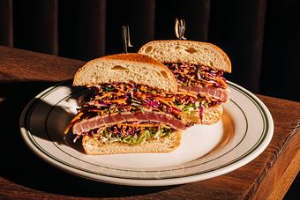 Product: A sandwich on a plate, filled with seared tuna, shredded vegetables, and garnishes, is cut in half and presented vertically. - Gus' Sip and Dip in Chicago, IL Restaurants/Food & Dining