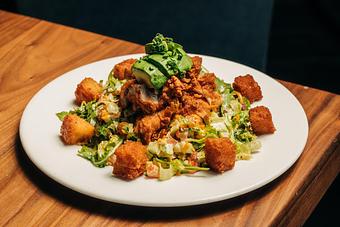 Product: chopped romaine and arugala are tossed with honey mustard dressing, tillamook cheese, bacon, tomato, cucumber, carrot. topped with buttermilk fried crispy chicken tenders, cornbread croutons, avocado, scallion - Hub 51 in River North - Chicago, IL American Restaurants