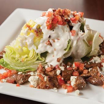 Product: Cajun seasoned steak tips served over a wedge of fresh lettuce topped with crisp bacon bits, bleu cheese dressing, diced tomatoes and bleu cheese crumbles. - Big Whiskey's American Restaurant & Bar in Springfield, MO American Restaurants