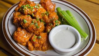 Product: White plate with a pile of chicken nuggets tossed in buffalo sauce, served with blue cheese dressing and celery - Bub City in Rosemont, IL Barbecue Restaurants