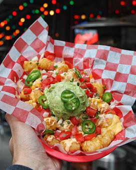Product: Tater tots served in a red basket on top of red checkered tissue paper and topped pico de gallo, jalapeno slices and a scoop of guacamole - Bub City in Rosemont, IL Barbecue Restaurants