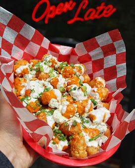 Product: Tater tots tossed in buffalo sauce served in a red basket on top of red checkered tissue paper and topped with ranch dressing drizzles and green onions - Bub City in Rosemont, IL Barbecue Restaurants