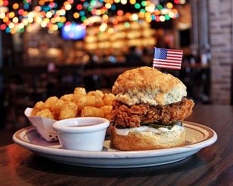 Product: Crispy fried chicken sandwich served on a biscuit with a side of tater tots and a ramekin of sauce - Bub City in Rosemont, IL Barbecue Restaurants