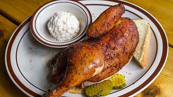 Product: Baked half chicken served on a white plate with a side of pickles and a ramekin of coleslaw - Bub City in Rosemont, IL Barbecue Restaurants