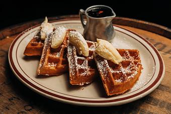 Product: Thick waffle cut into fourths on a white plate, each slice topped with butter and powdered sugar - Bub City in Rosemont, IL Barbecue Restaurants
