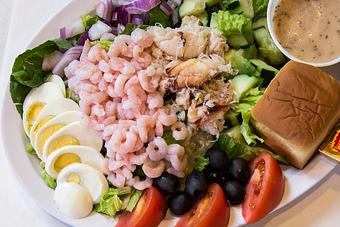 Product: Oregon shrimp meat and Dungeness crab meat on a classic salad with hardboiled egg, black olives, tomato, cucumber and red onion! - Fisherman's Market in Whiteaker - Eugene, OR Seafood Restaurants