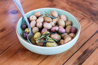 Product: Green and purple olives in a small white dish with a spoon on a wooden table - Lil’ Ba-Ba-Reeba! in River North - Chicago, IL Bars & Grills