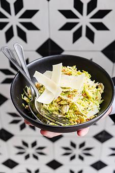 Product: Three green shredded Brussels sprouts topped with cheese shavings in a grey bowl with a fork and a spoon, being held by a caucasian hand in front of a black and white tiled background - Lil’ Ba-Ba-Reeba! in River North - Chicago, IL Bars & Grills