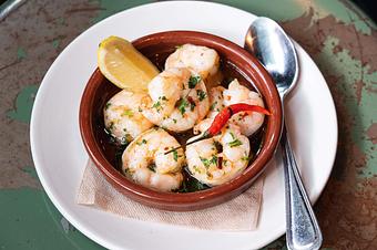 Product: White shrimp with a red pepper and a lemon wedge in a round brown dish on a white dish, sitting on a wooden surface - Lil’ Ba-Ba-Reeba! in River North - Chicago, IL Bars & Grills