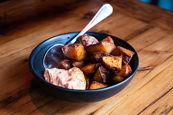Product: Brown fried potato chunks served with an orange sauce and a silver spoon on a small white plate served on a wooden table - Lil’ Ba-Ba-Reeba! in River North - Chicago, IL Bars & Grills