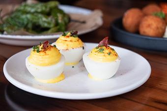 Product: Three hard boiled egg halves on a white plate, filled with creamy yellow yolks, topped with red spices and cured meat - Lil’ Ba-Ba-Reeba! in River North - Chicago, IL Bars & Grills