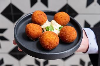 Product: Four golden balls on a white sauce with a green herb garnish on a small black plate in front of black and white patterned tiles - Lil’ Ba-Ba-Reeba! in River North - Chicago, IL Bars & Grills