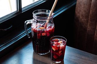 Product: A clear glass pitcher of red liquid next to a large clear glass of the same red liquid with ice and garnished with pieces of fruit - Lil’ Ba-Ba-Reeba! in River North - Chicago, IL Bars & Grills