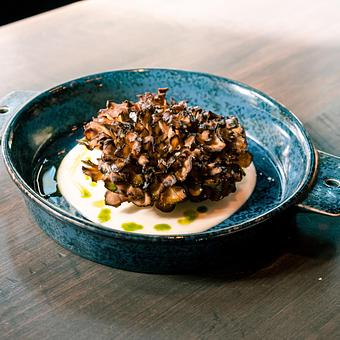 Product: Brown roasted Hen of the Woods mushrooms in a pool of white sauce in a black bowl, on a wooden table top - Lil’ Ba-Ba-Reeba! in River North - Chicago, IL Bars & Grills