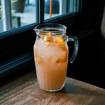 Product: A large clear pitcher filled with a peach colored liquid and ice, topped with pieces of fruit, on a wooden table in front of a window - Lil’ Ba-Ba-Reeba! in River North - Chicago, IL Bars & Grills