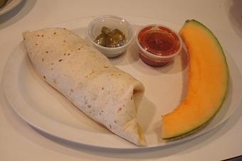Product: Two eggs scrambled, sausage, homemade green salsa, onion & cheese in a flour tortilla served with fresh fruit. - Nutshell Eatery & Bakery in Granbury, TX American Restaurants
