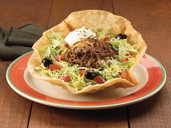 Product: Tame your appetite with this tostada filled with your choice of meat mixed with Spanish rice and mild Cheddar and Monterey Jack cheese on a crip tortilla covered with shredded lettuce, tomatoes, black olives and a scoop of sour cream topping. - Paradiso Mexican Restaurant in Minot, ND Mexican Restaurants