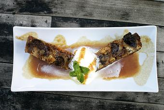 Product: Flambéed black mission figs and golden raisin packed bread pudding loaded with vanilla custard finished with whip and rum caramel. - PUBlic 74 in San Juan Capistrano, CA American Restaurants