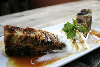 Product: Flambéed black mission figs and golden raisin packed bread pudding loaded with vanilla custard finished with whip and rum caramel - PUBlic 74 in San Juan Capistrano, CA American Restaurants