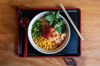 Product: our classic chicken broth with a green curry miso, served with tokyo wavy noodles, featuring butter poached shrimp, fresh herbs, green onions and buttered corn, all topped with chili threads, rayu and a squeeze of lime - RAMEN-SAN Whisky Bar in Fulton Market - Chicago, IL Japanese Restaurants
