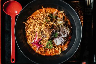 Product: from our collaboration with pink salt, this bowl features a rich coconut curry broth, beef is braised with lemongrass and muskrat lime until tender, topped with crispy noodles, pickled vegetables, and fresh herbs - RAMEN-SAN Whisky Bar in Fulton Market - Chicago, IL Japanese Restaurants