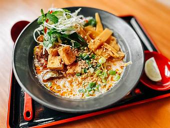 Product: Variation of a traditional Tom Kha features a rich coconut broth, fried Thai eggplant and tofu, cabbage and herb salad with lemongrass, Thai basil, mint, cilantro and fresnos, marinated bamboo shoots, served with makrut lime and fried garlic. - RAMEN-SAN Whisky Bar in Fulton Market - Chicago, IL Japanese Restaurants