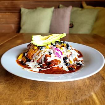 Product: Roasted vegetables, black beans, corn, salsa and cheese in blue corn tortillas. Smothered in red or green chile and topped with lime crema and salsa. Served with tortilla chips and salsa. - The Acre in Albuquerque, NM American Restaurants