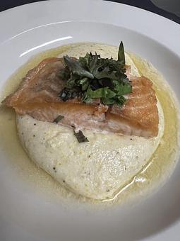 Product: Pan-seared salmon with sautéed spinach and creamy grits, finished in a caper-cream sauce. - The Bowman in Parkville, MD American Restaurants