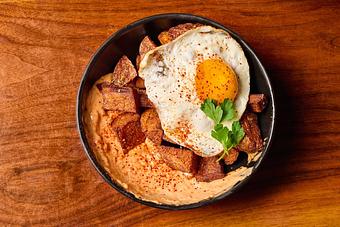 Product: A black dish with an orange sauce, a fried egg with a bright yellow center, golden potato pieces and a green garnish, on a wooden table - Lil’ Ba-Ba-Reeba! in River North - Chicago, IL Bars & Grills
