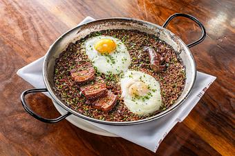 Product: A brown rice dish topped with meats and eggs in a skillet on a wooden table - Lil’ Ba-Ba-Reeba! in River North - Chicago, IL Bars & Grills