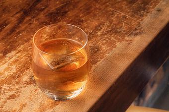 Product: Light brown liquid in a short clear glass with a square ice cube, on a wooden bar top - Lil’ Ba-Ba-Reeba! in River North - Chicago, IL Bars & Grills
