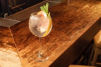 Product: A clear liquid with ice in a large globe wine glass, garnished with a grapefruit slice and green herbs, on a wooden bar top - Lil’ Ba-Ba-Reeba! in River North - Chicago, IL Bars & Grills