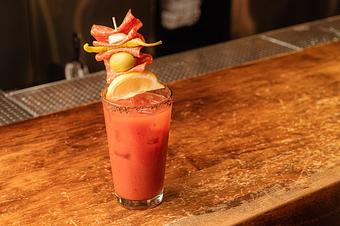 Product: Red liquid in a tall glass with ice, with brown salt and spice on the rim, garnished with meats, pepper, an olive and a lemon wedge - Lil’ Ba-Ba-Reeba! in River North - Chicago, IL Bars & Grills