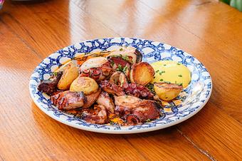 Product: Roasted pieces of octopus mixed with roasted potatoes, garnished with chives, on a patterned blue and white plate on a wooden table - Lil’ Ba-Ba-Reeba! in River North - Chicago, IL Bars & Grills