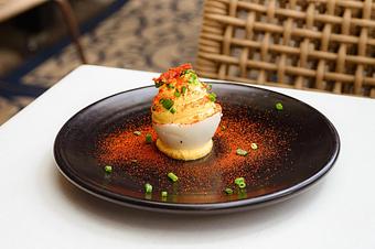 Product: Half of a hard boiled egg with a dollop of yellow filling, garnished with orange paprika and green chives, on a black plate - Lil’ Ba-Ba-Reeba! in River North - Chicago, IL Bars & Grills