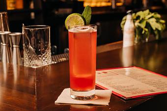 Product: A red liquid with a large rectangular ice cube in a tall clear collins glass, garnished with a lime wedge and green herbs - Lil’ Ba-Ba-Reeba! in River North - Chicago, IL Bars & Grills