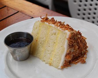 Product: triple layer coconut vanilla cake with coconut buttercream and white chocolate shavings. served with a side of chocolate sauce - Hub 51 in River North - Chicago, IL American Restaurants