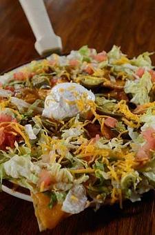 Product: Individual tostada chips piled high with refritos and topped with melted cheese. the dish is sprinkled with jalapeño slices and set off by a garnish of lettuce, bits of tomato, and a dab of sour cream. - Papa Felipe's in Albuquerque, NM Mexican Restaurants