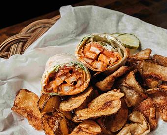 Product: a buffalo chicken wrap cut in half served on a pile of potato chips in a basket with white parchment paper - RJ Grunts in Lincoln Park - Chicago, IL American Restaurants