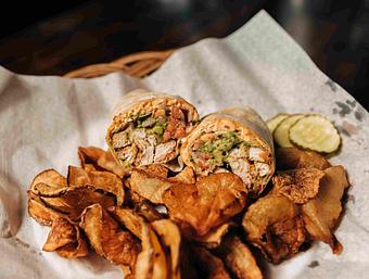 Product: a Santa Fe wrap cut in half served on a pile of potato chips with a side of sliced pickles - RJ Grunts in Lincoln Park - Chicago, IL American Restaurants