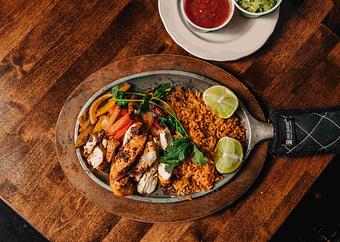 Product: a sizzling pan of chicken fajitas with sliced lime wheels and peppers on a brown table - RJ Grunts in Lincoln Park - Chicago, IL American Restaurants