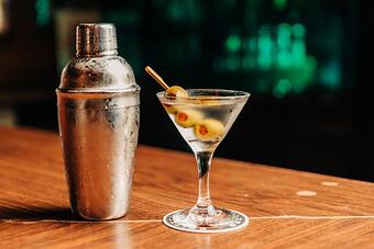 Product: a dirty vodka martini in a martini glass with three olives on a toothpick as a garnish next to a cocktail shaker - RJ Grunts in Lincoln Park - Chicago, IL American Restaurants