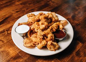 Product: A white plate with crispy chicken tenders, served with a small cup of ranch dressing and a side of ketchup - RJ Grunts in Lincoln Park - Chicago, IL American Restaurants
