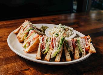 Product: A sandwich with turkey, bacon, lettuce, tomato, and mayonnaise on toasted brioche bread, served with cottage fries and pickle slices on a white plate on a wooden table - RJ Grunts in Lincoln Park - Chicago, IL American Restaurants