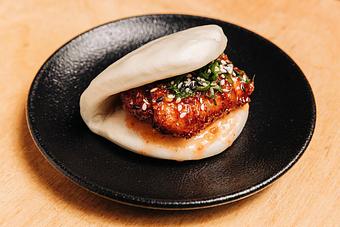 Product: limited edition: a play on everyone's favorite chinese-american dish, fried chicken tossed in orange sauce, served with black and white sesame seeds, scallion and cilantro on a steamed bun - RAMEN-SAN Whisky Bar in Fulton Market - Chicago, IL Japanese Restaurants