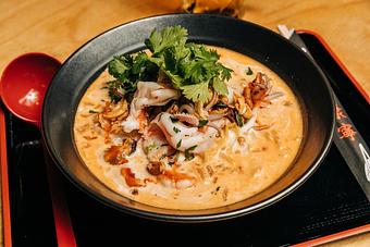 Product: A play on the Brazilian seafood stew made in collaboration with Chef John Manion (Brasero & El Che) featuring Tantan broth, coconut cream, tokyo wavy noodles, cod, squid, shrimp, mussels, Chef John's hot sauce, cashews, fried shallots & cilantro. - RAMEN-SAN Whisky Bar in Fulton Market - Chicago, IL Japanese Restaurants