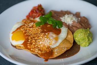 Product: Fried eggs, crispy tortilla, black bean purée, chile morita sauce, queso fresco, guacamole, pico de gallo and refried beans. - Red Mesa Restaurant in St Petersburg, FL Mexican Restaurants